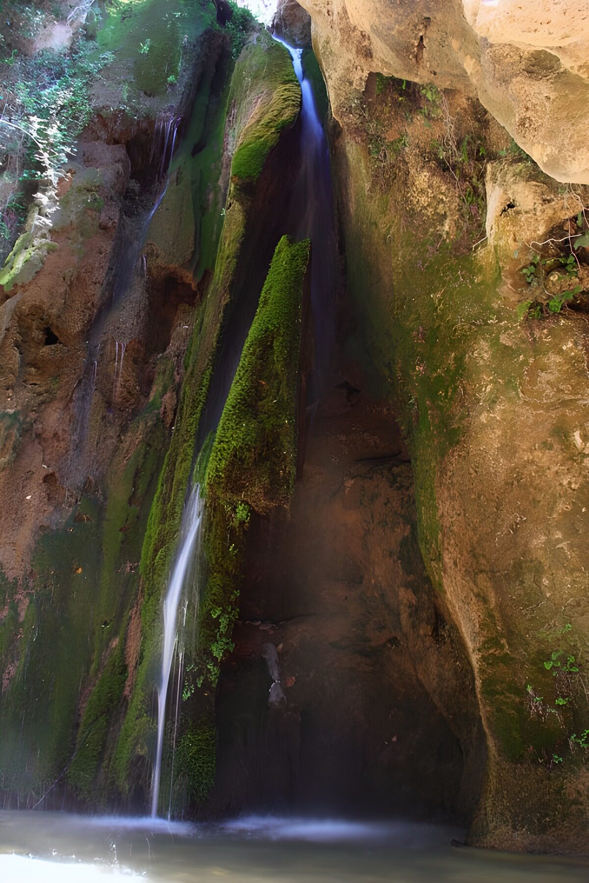 Smalle waterval langs groene rotsen