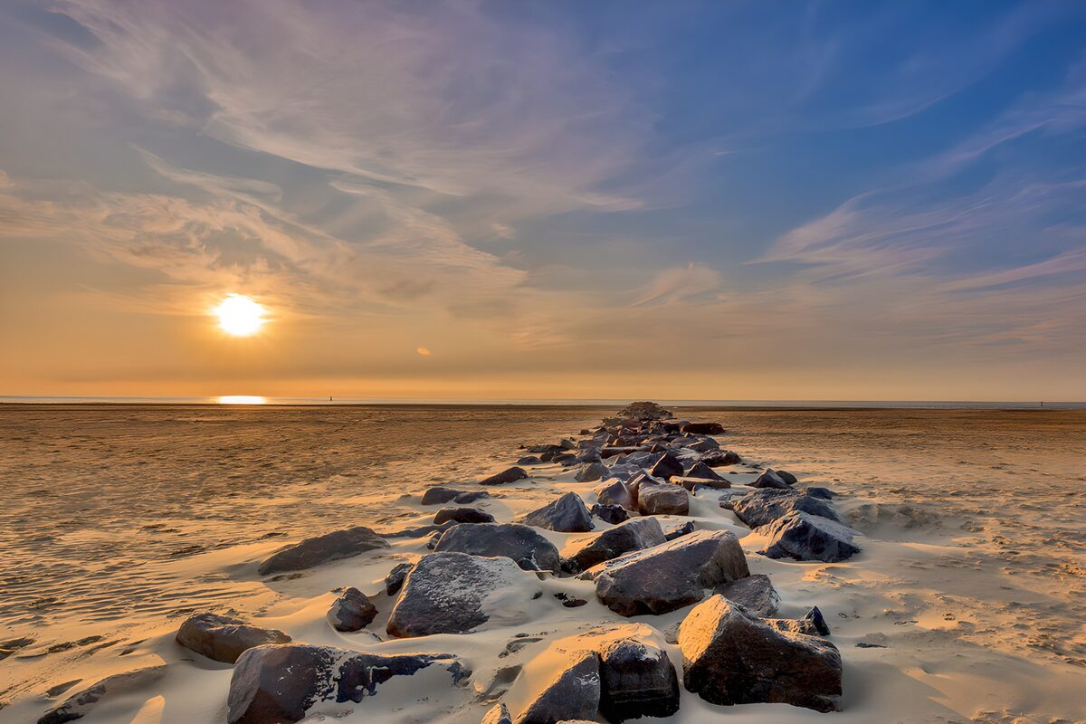 Zonsondergang boven strand en golfbreker