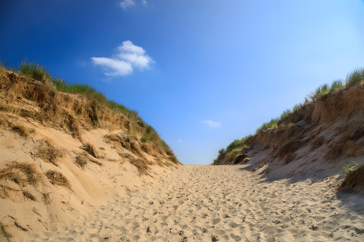Zandpad tussen duinen onder blauwe lucht