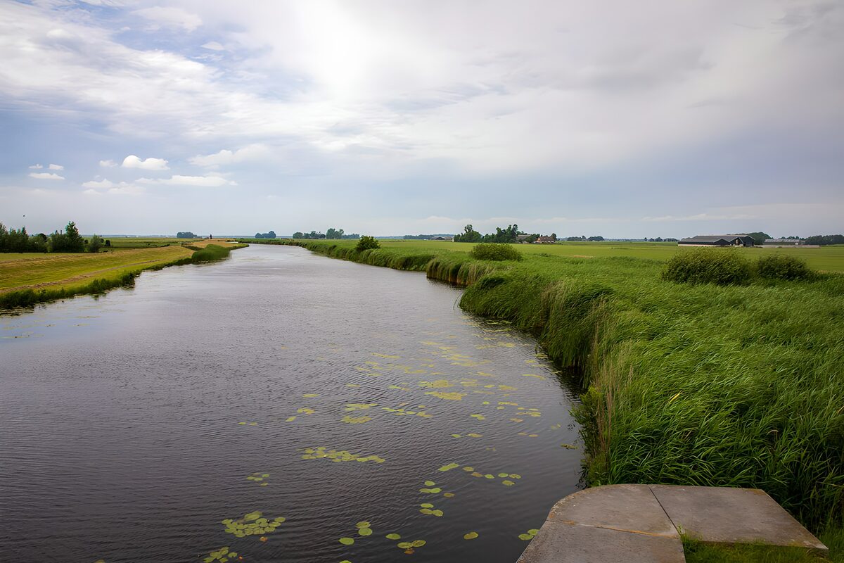 Brede watergang tussen groene weilanden